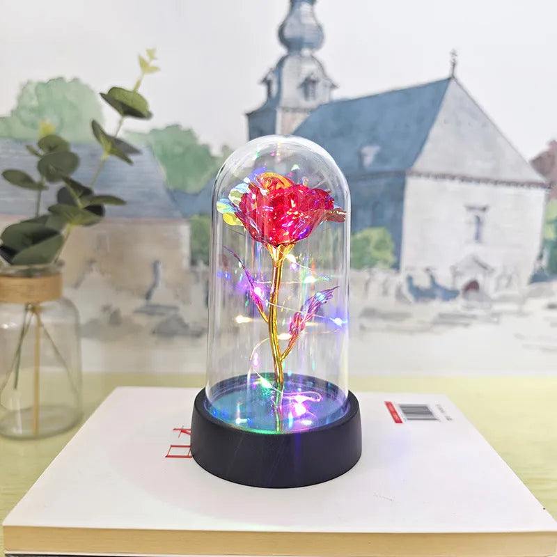 Small decorative table lamp with coloured LED lights illuminating plastic flowers under a glass dome.