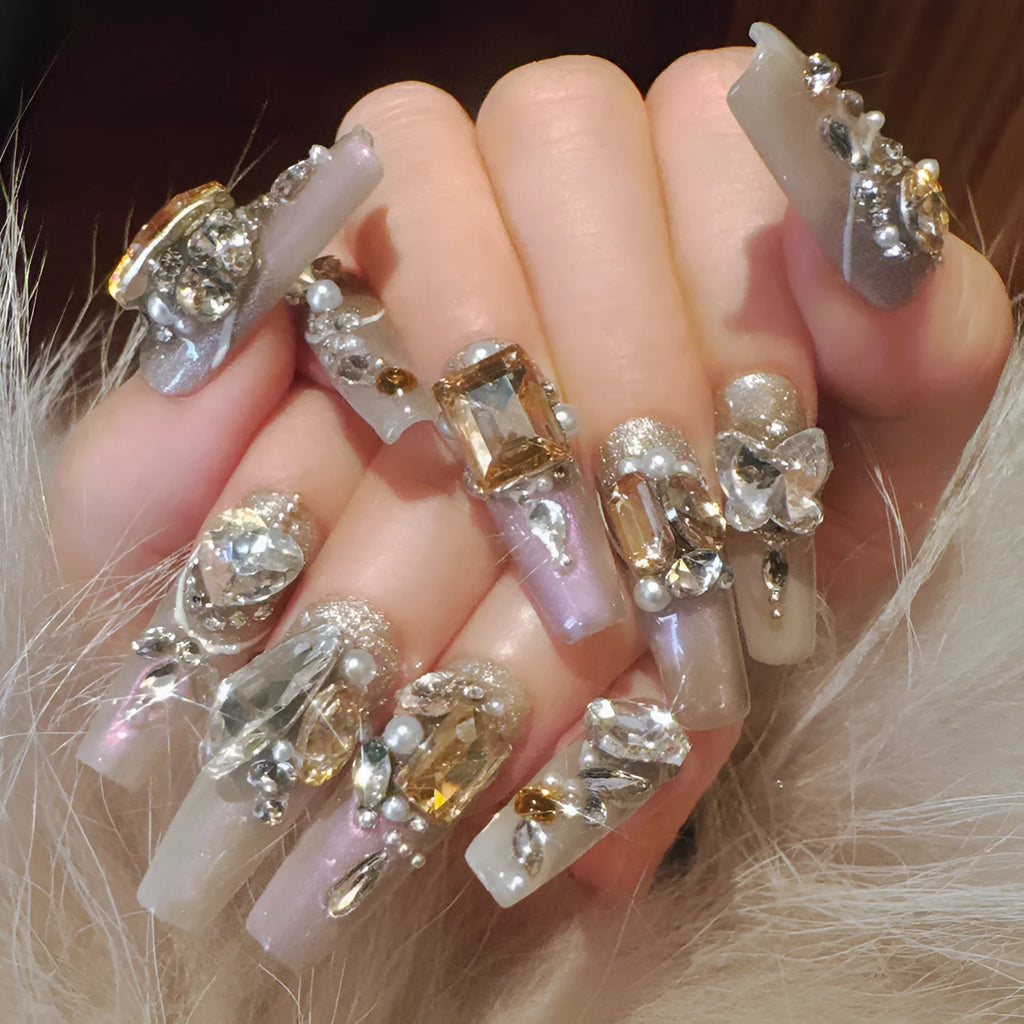 Ten false nail patches with rhinestones on a card, next to jelly adhesive and manicure tools.