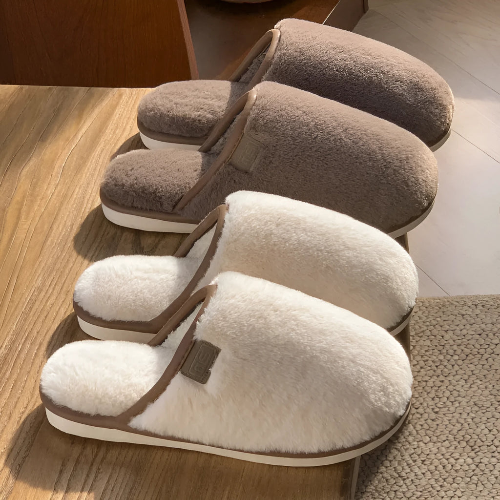 Pair of solid colour plush house slippers with PVC sole on a wooden floor.