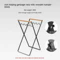Black iron folding trash storage rack with wooden handle mounted on a wall.