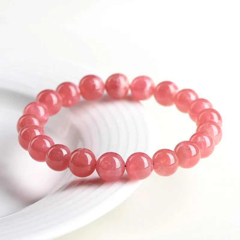 Women's geometric rhodochrosite crystal bracelet with a longevity lock charm on a wrist.