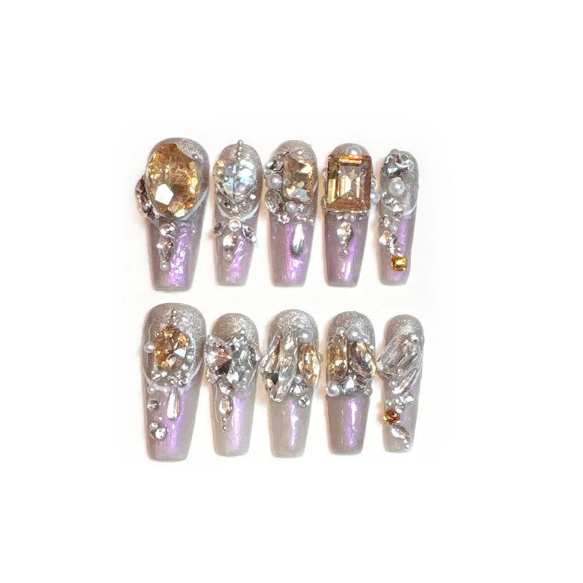 Ten false nail patches with rhinestones on a card, next to jelly adhesive and manicure tools.
