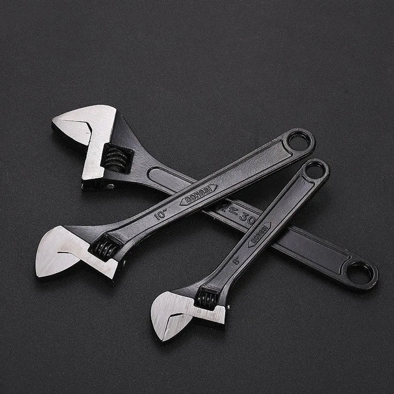 Blackened high-carbon steel adjustable open-end wrench with ergonomic handle on a workbench.