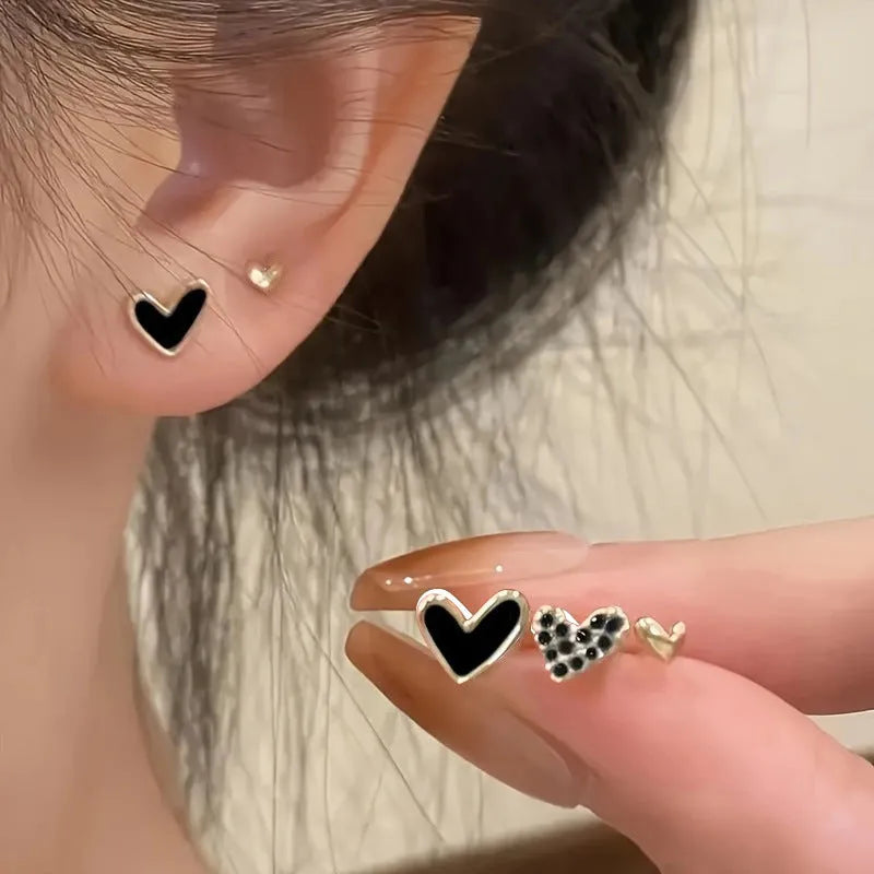 Three pairs of women's heart-shaped alloy earrings in gold, black, white, and pink colours