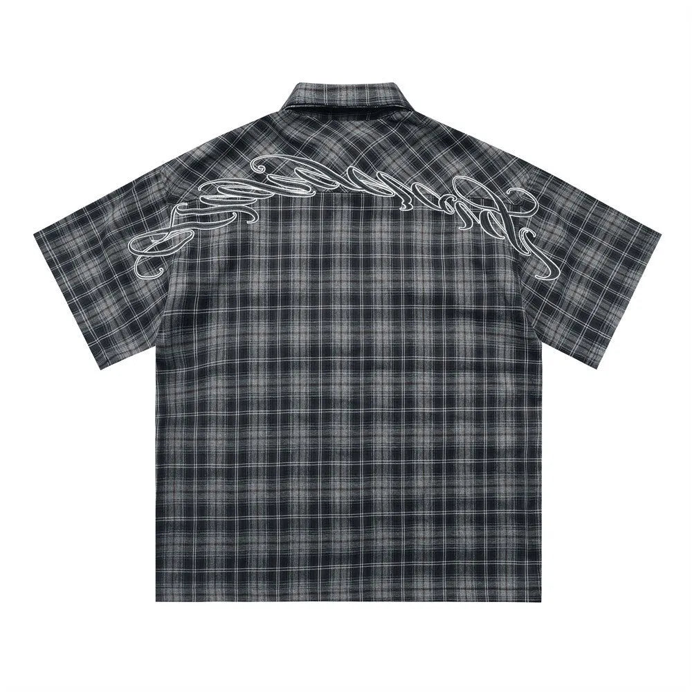 Man wearing a black and brown plaid short sleeve shirt with embroidered letter on lapel