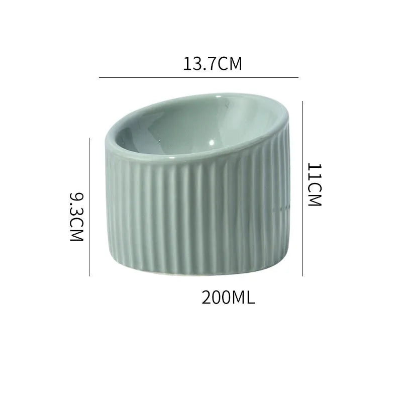 A dark green ceramic elevated cat bowl on a wooden surface, showing its tilted, round shape.