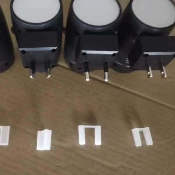 A compact white plug-in night lamp with a rotatable head, shown plugged into a wall socket.