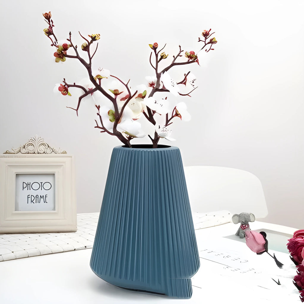 Simple plastic decorative flower vase in blue, green, pink, or white on a desktop.