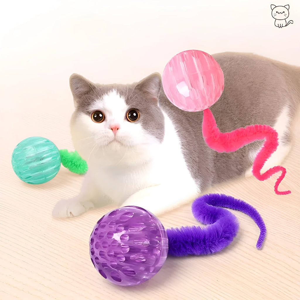 Green TPR bouncy ball with pink plush worm tail cat toy on floor