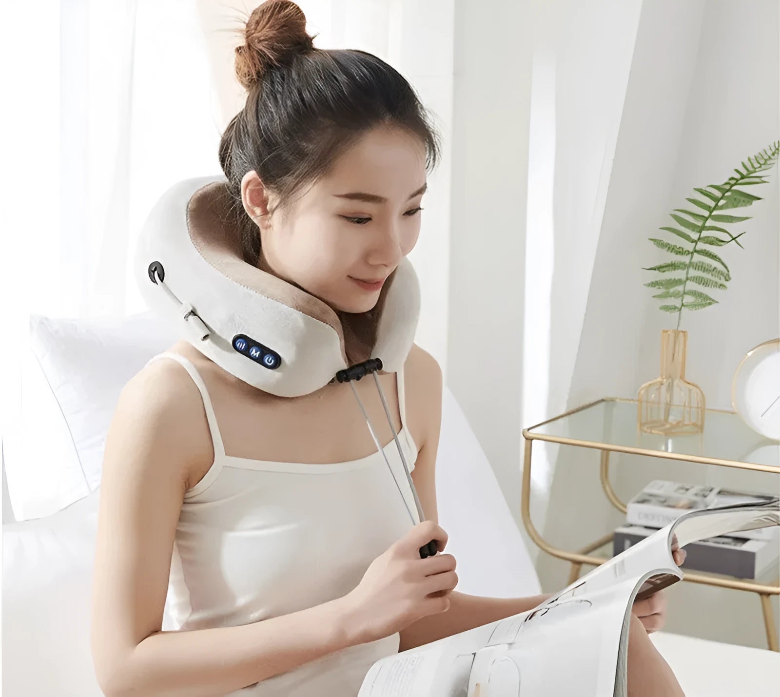 Brown U-shaped electric neck massage pillow with control buttons, shown on a table.