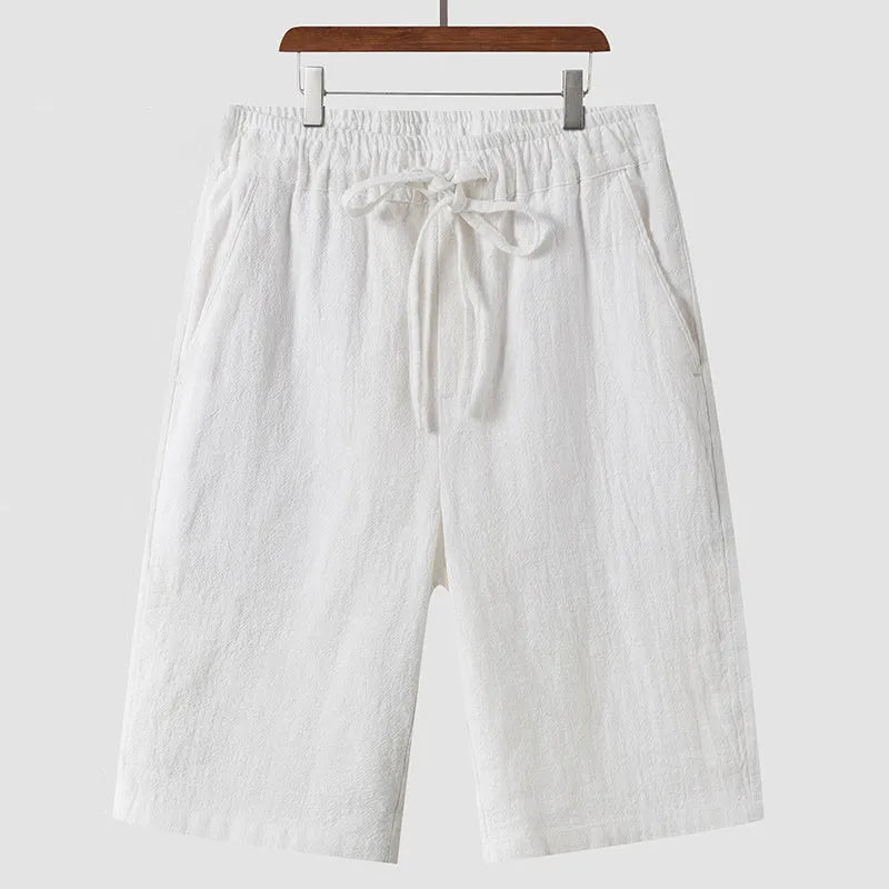 Men's beige linen casual shorts with a loose fit and cropped length on a plain background.