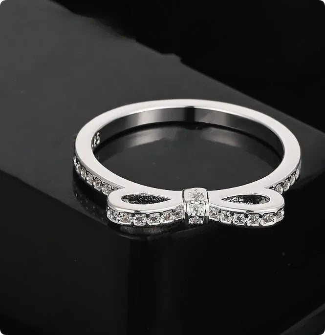 Silver coloured bow-shaped ring with zircon crystal details on a white background.