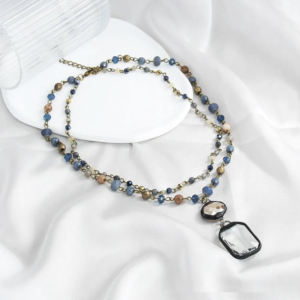 Two-layer tribal necklace with stone and glass pendants on a chain, shown in beige and blue.