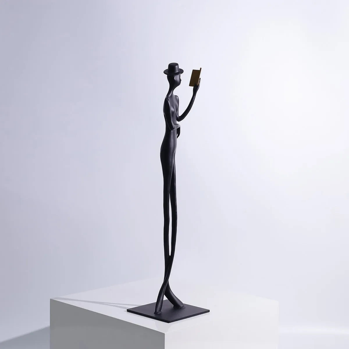 Black metal sculpture of a seated woman reading a book, modern minimalist desk decor.