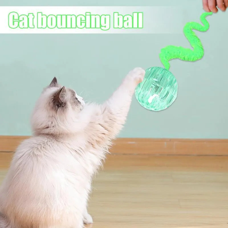 Green TPR bouncy ball with pink plush worm tail cat toy on floor
