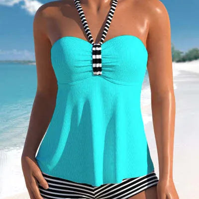 Woman modelling a black and white striped off-shoulder one-piece swimsuit on a beach.