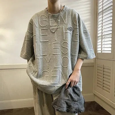 Man wearing a grey loose-fit T-shirt with a raised 3D retro letter print on the front.
