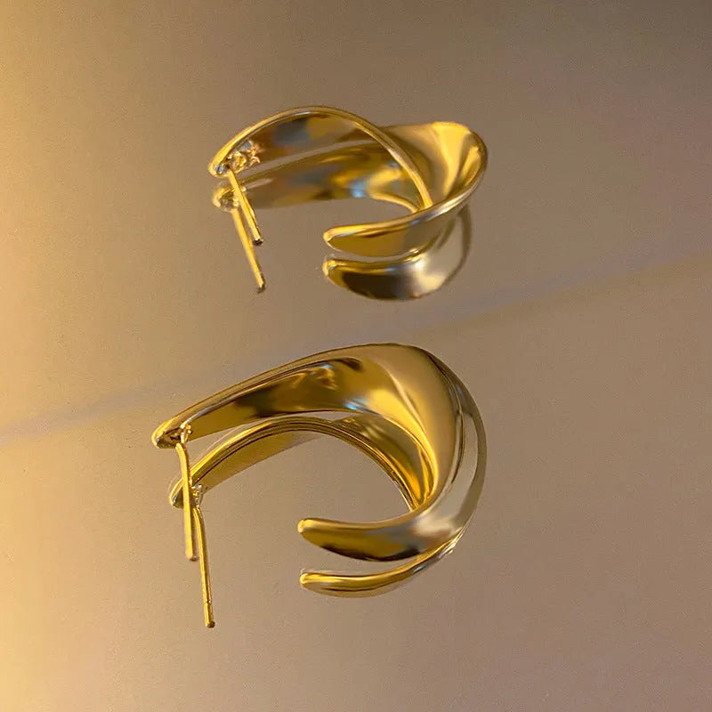 A pair of geometric twisted metal earrings with a round shape in a gold colour.