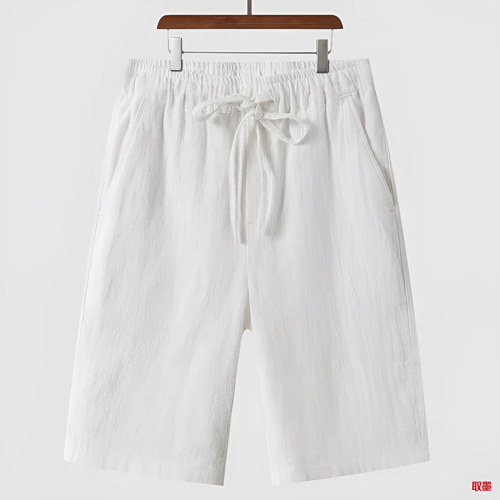 Men's beige linen casual shorts with a loose fit and cropped length on a plain background.