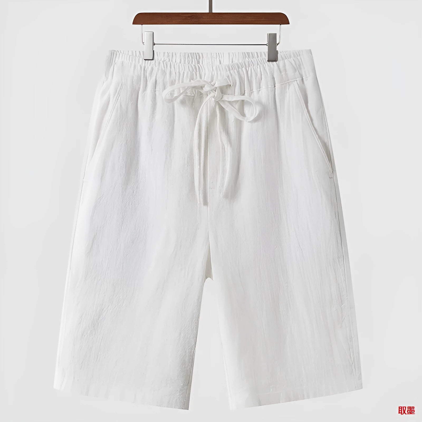 Men's beige linen casual shorts with a loose fit and cropped length on a plain background.