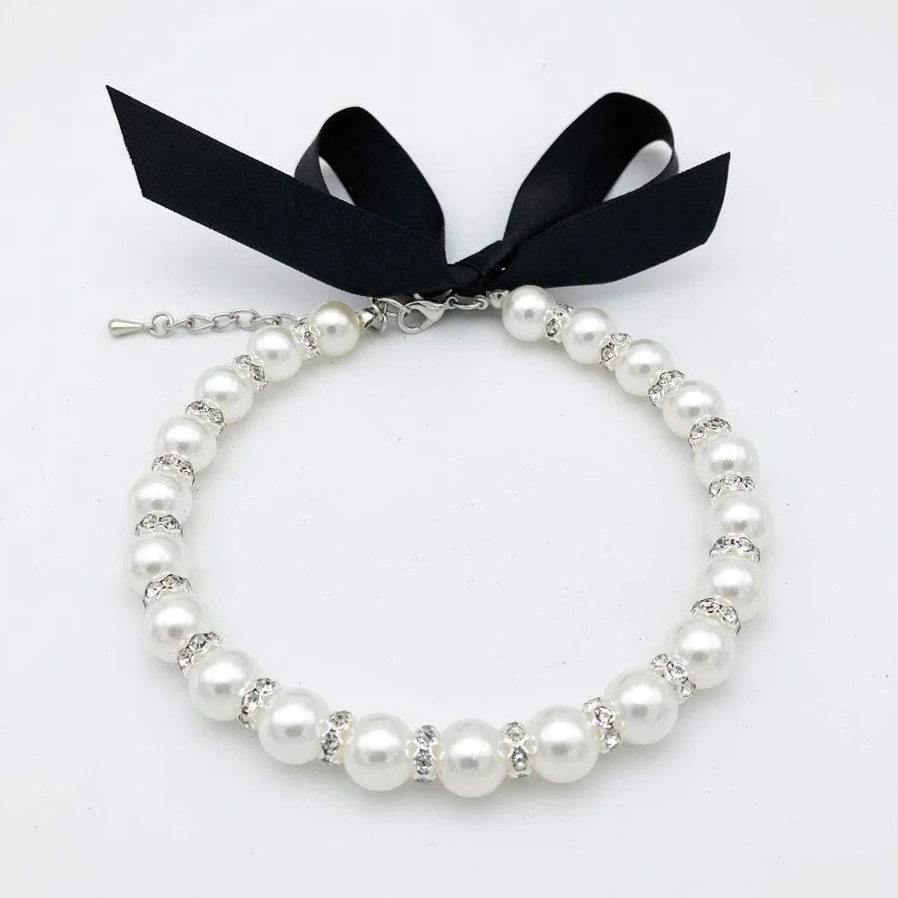 Small dog wearing a blue pearl and rhinestone necklace with a ribbon bow.