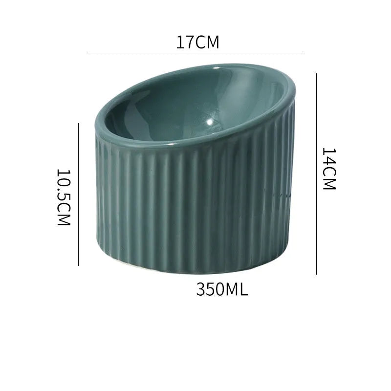 A dark green ceramic elevated cat bowl on a wooden surface, showing its tilted, round shape.