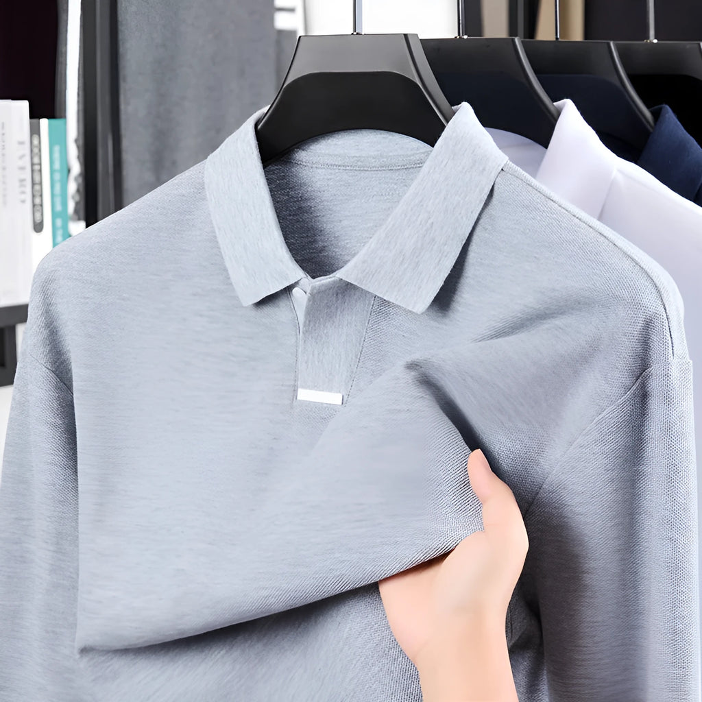 Man wearing a loose grey cotton polo shirt with a lapel collar and asymmetric design detail.