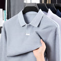 Man wearing a loose grey cotton polo shirt with a lapel collar and asymmetric design detail.
