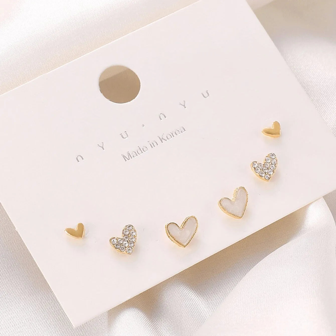 Three pairs of women's heart-shaped alloy earrings in gold, black, white, and pink colours