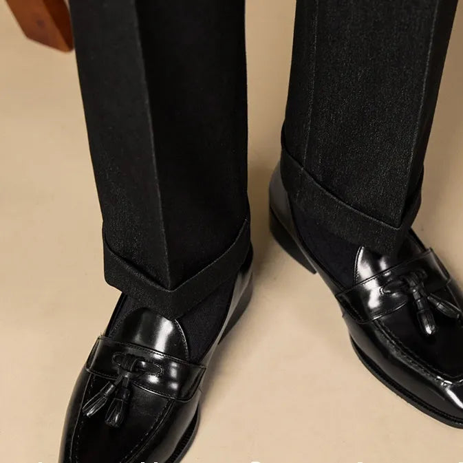 Men's black polished leather tassel loafers with a rubber sole on a white background.