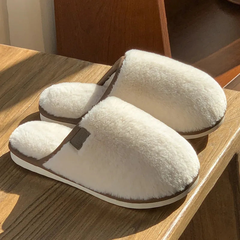 Pair of solid colour plush house slippers with PVC sole on a wooden floor.