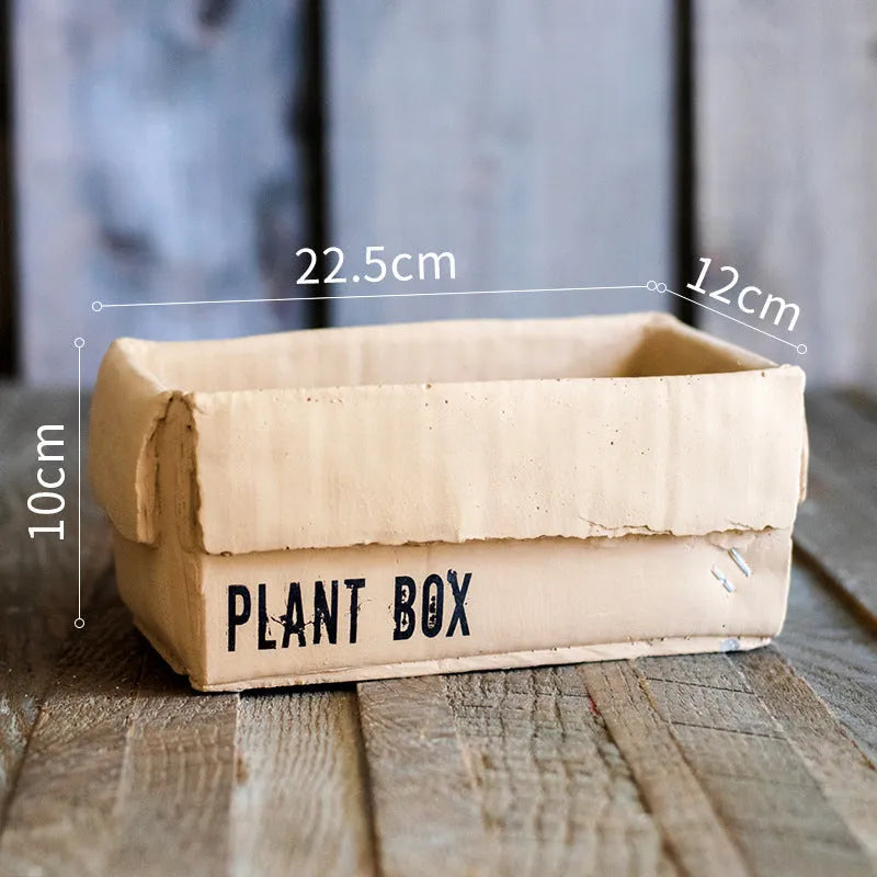 Cement flowerpot with brown paper box design on a floor, showing pre-perforated drainage holes.