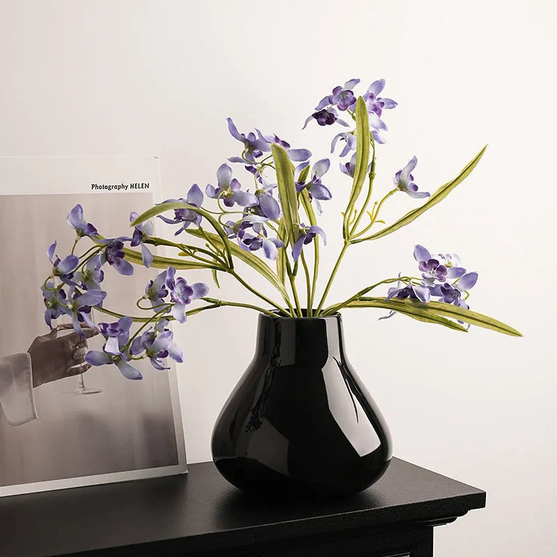 Ceramic decorative vase with coloured glaze surface and artificial orchid flowers in black or white colour