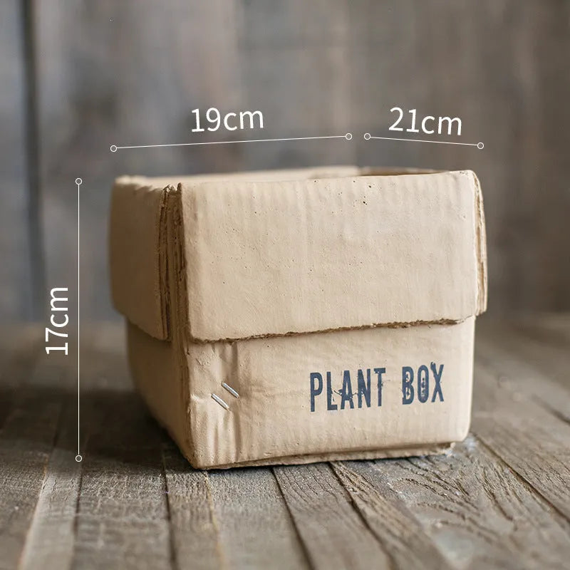 Cement flowerpot with brown paper box design on a floor, showing pre-perforated drainage holes.