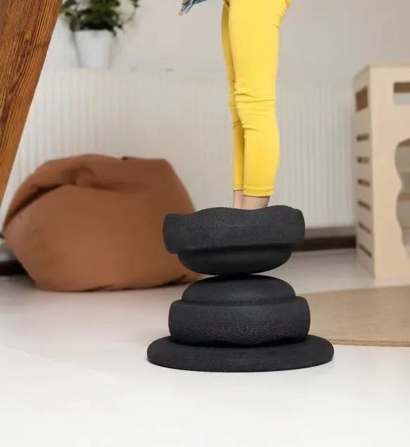 Plastic surfboard-shaped balance board for children, shown in mixed wood colour and black options.