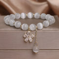 White cat's eye crystal bracelet for women with a small flower tassel and a morganite-coloured safety buckle.