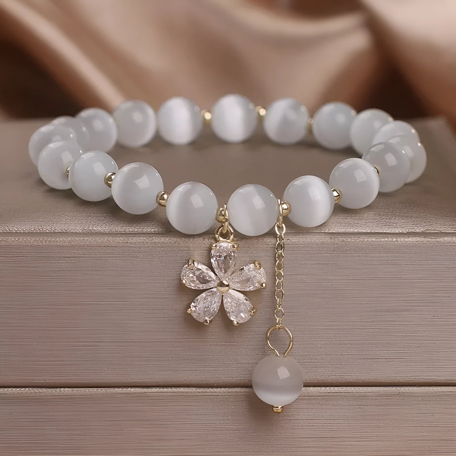 White cat's eye crystal bracelet for women with a small flower tassel and a morganite-coloured safety buckle.