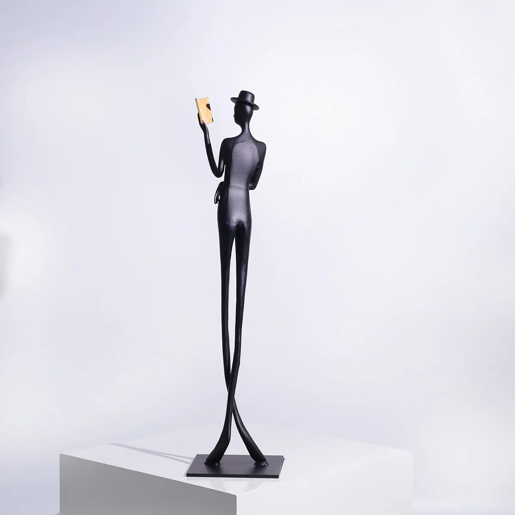 Black metal sculpture of a seated woman reading a book, modern minimalist desk decor.