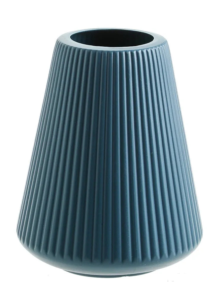 Simple plastic decorative flower vase in blue, green, pink, or white on a desktop.