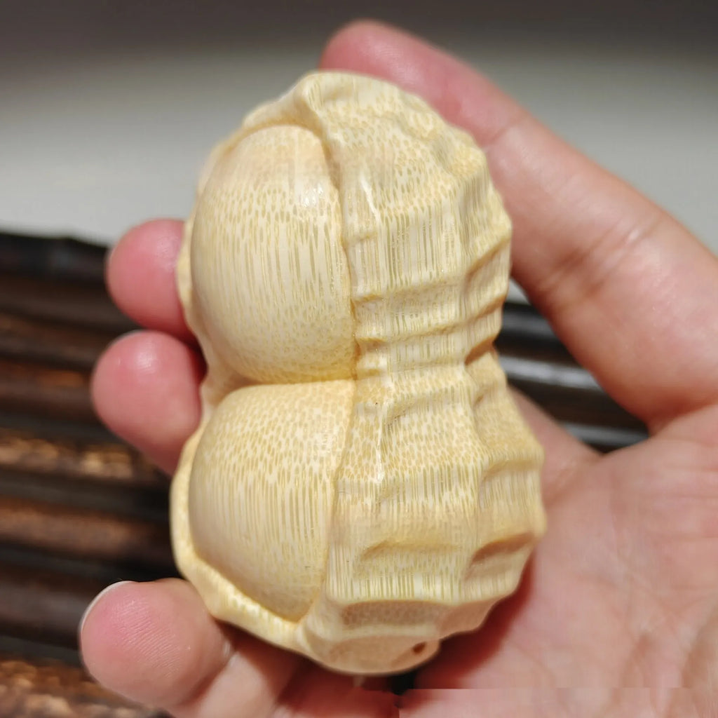 Solid natural bamboo ornament carved into a peanut shape on a plain background.
