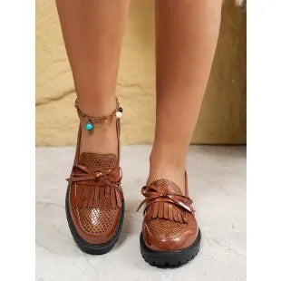 Brown women's slip-on loafers with a black bow detail on the front.