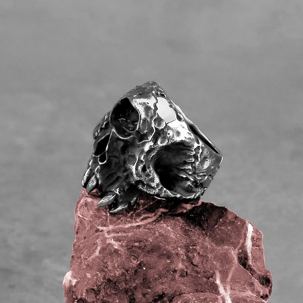 A silver-toned alloy ring with a raised one-eyed skull design on a black background.