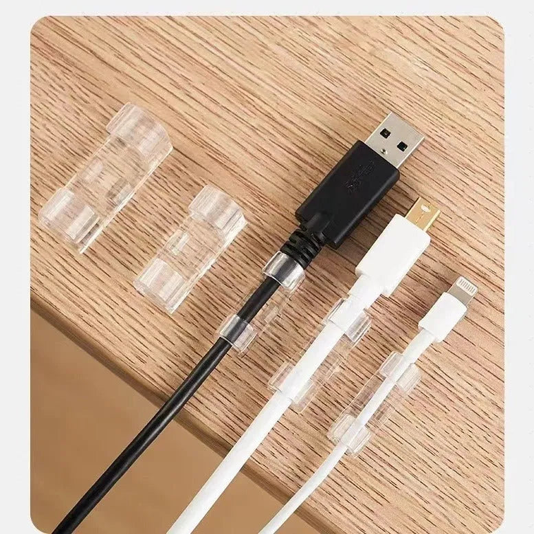 Transparent plastic self-adhesive cable clip holding a white wire against a wall.