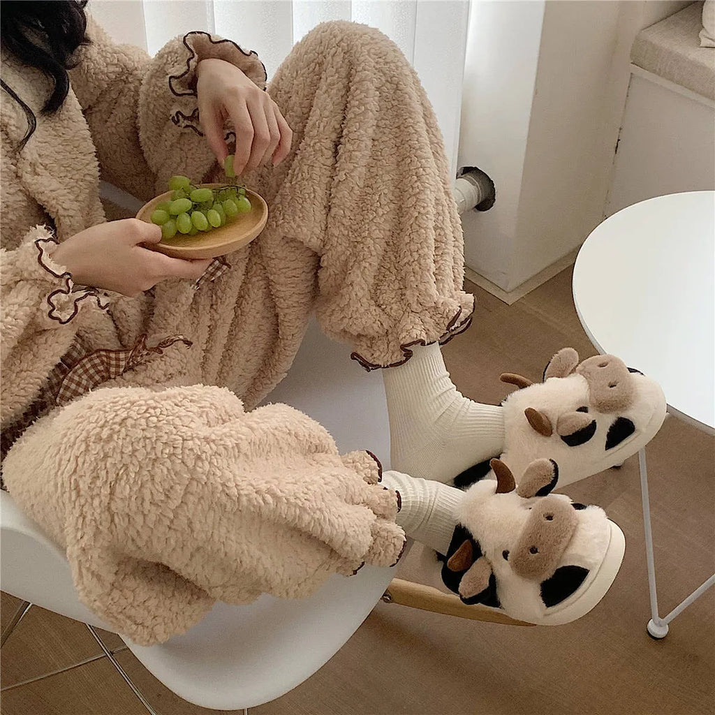 White cartoon cow plush house slippers for women with a non-slip textured sole.