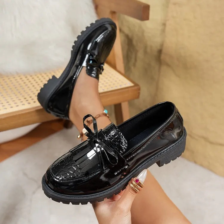 Brown women's slip-on loafers with a black bow detail on the front.