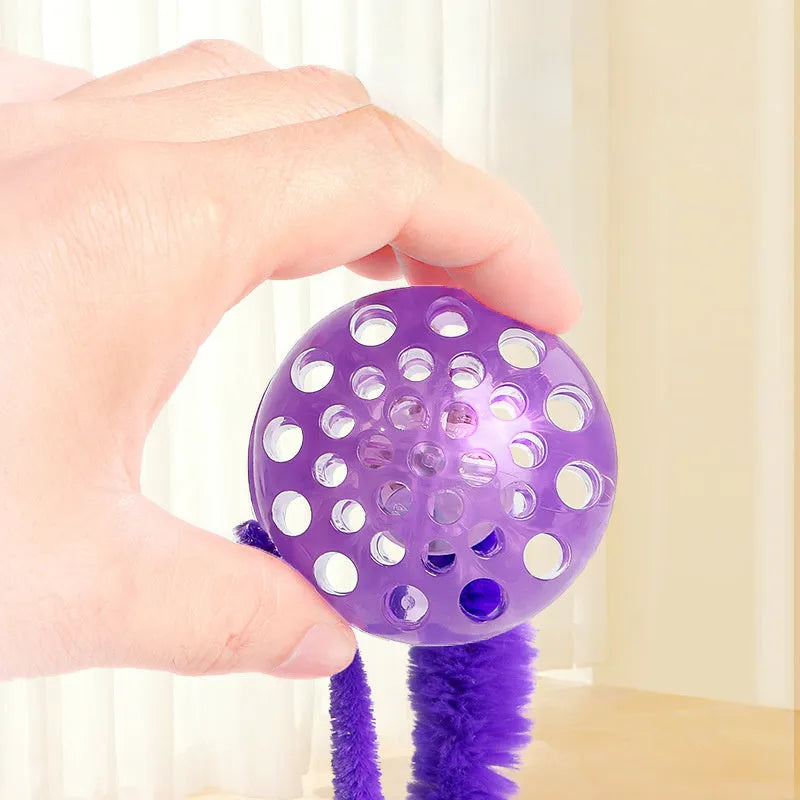 Green TPR bouncy ball with pink plush worm tail cat toy on floor
