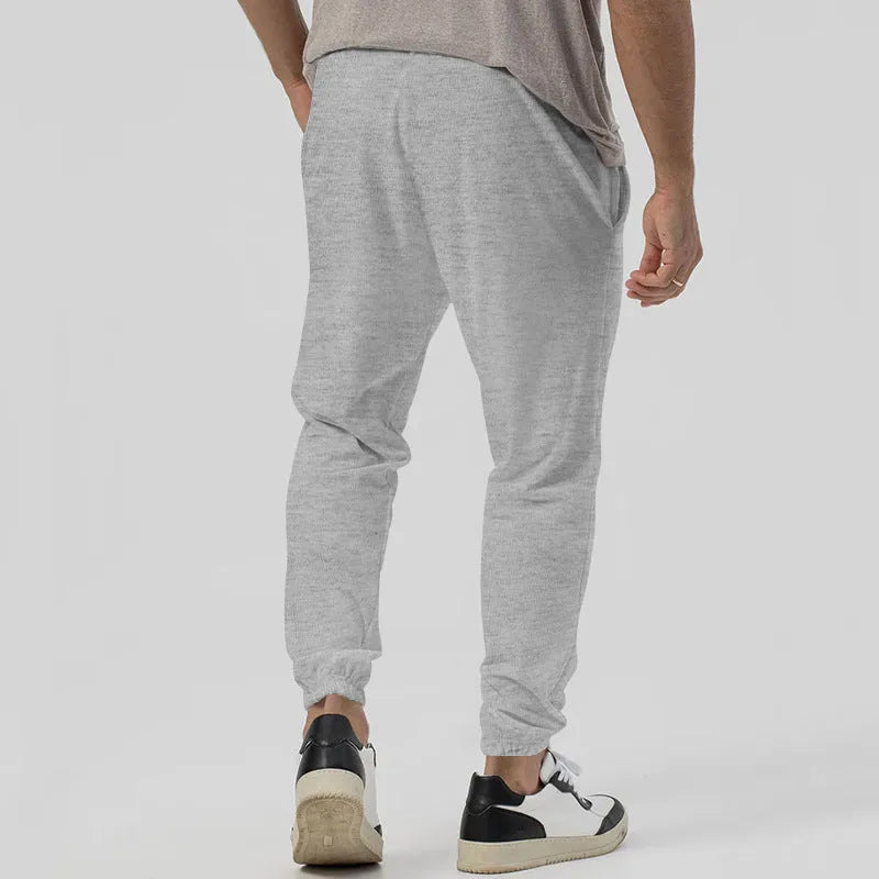 Men's grey loose tapered track sweatpants with elastic waist and straight leg design.